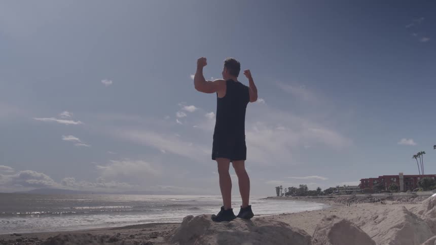 Man in sportswear standing on rocks with arms raised at the beach