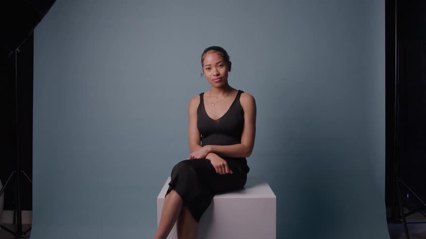 Woman sitting on a white cube in front of a blue studio backdrop