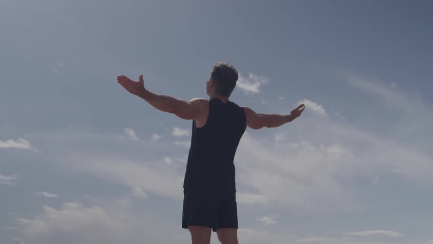 Man stands outside and raises his arms in the air as his shirt ripples in the wind