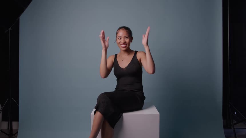 Woman smiles with raised hands in playful gesture against blue backdrop in studio