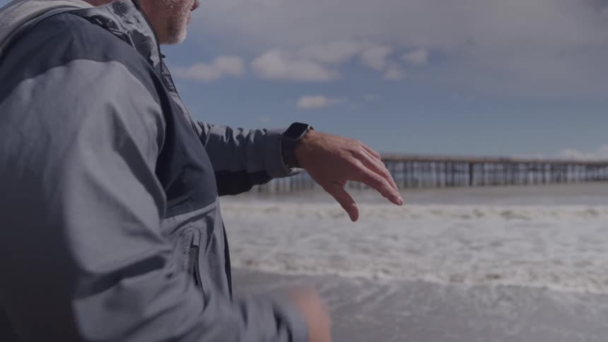 A man standing at the beach looking at his watch