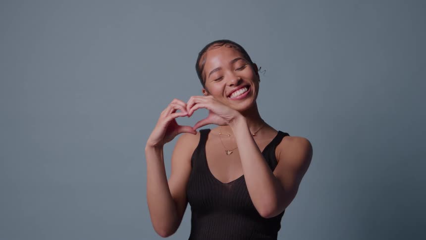 Woman makes heart gesture with hands against bluegray background