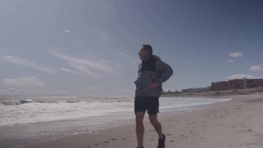 A middle aged man jogging outdoors along the ocean coast during daytime