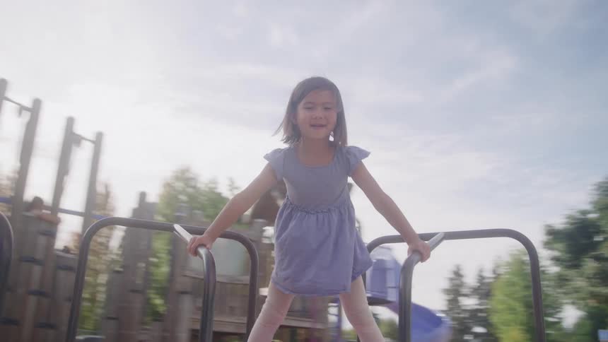 Child holds metal bars on playground structure under blue sky with trees in background