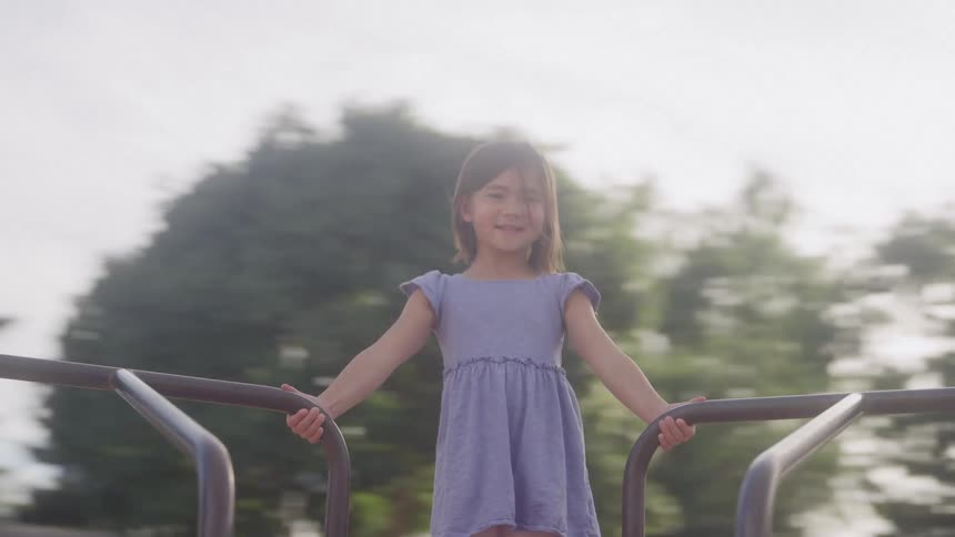 A female child standing on a rotating ride in an outdoor play area during daytime