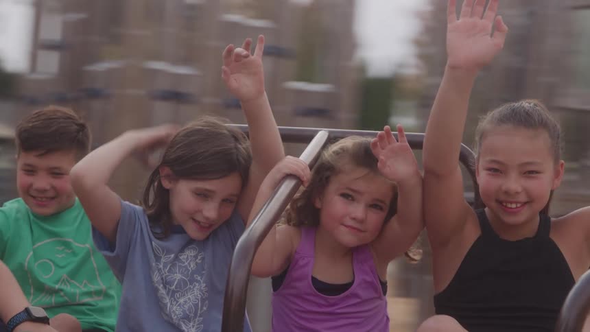 Four children enjoy merrygoround ride with raised hands and cheerful smiles