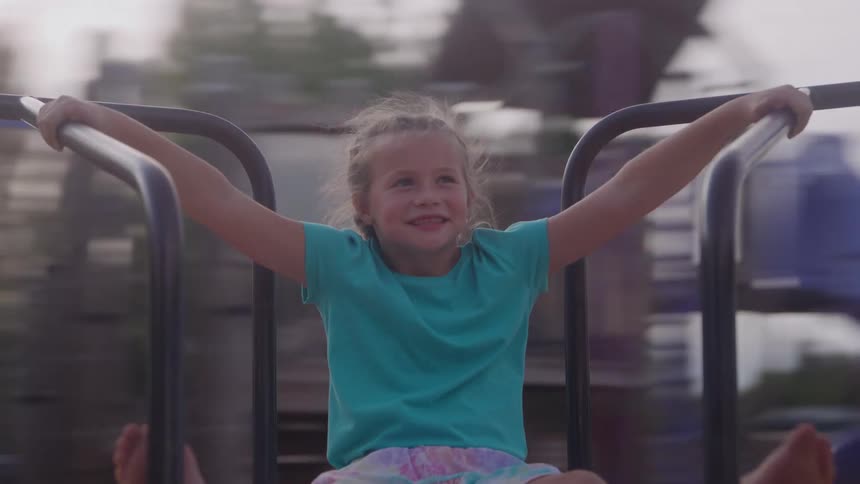 A young girl clings to a spinning playground wheel her face lit with excitement as it whirls rapidly under the midday sun
