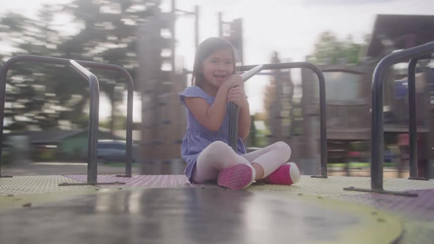 Girl sitting on a spinning playground ride holding a metal bar