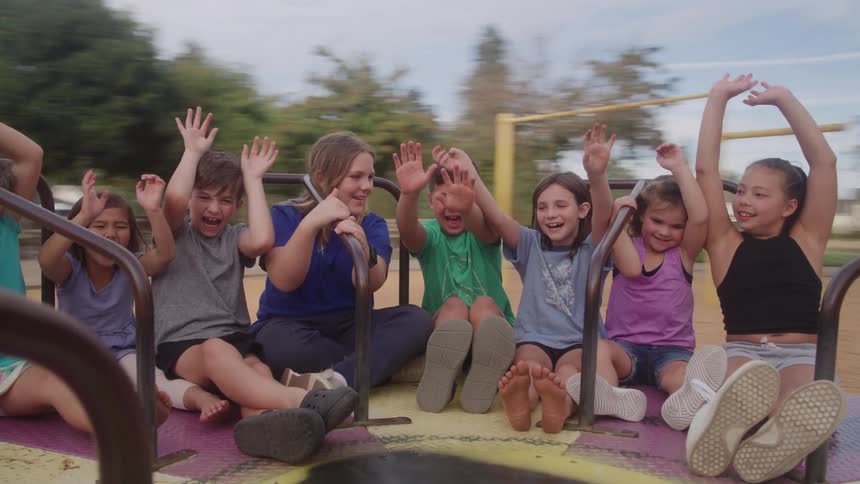 Children enjoy playground merrygoround smiling and raising hands during the ride