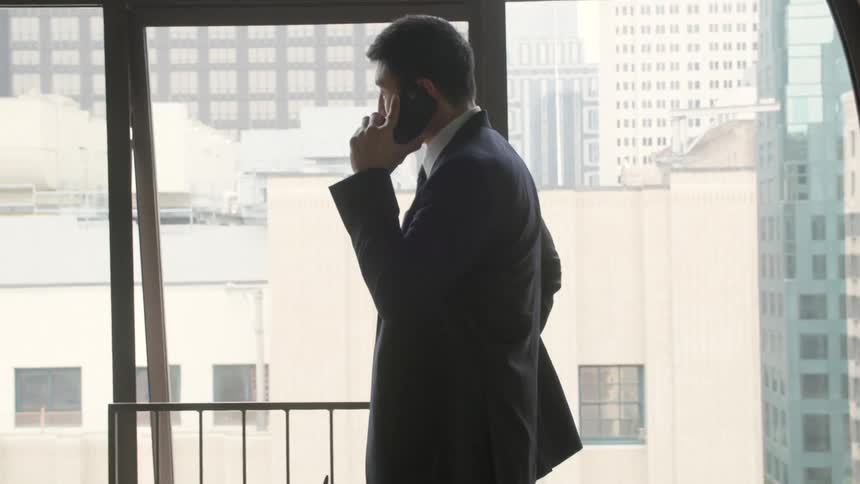 Man in a suit on a phone call in front of a cityview window