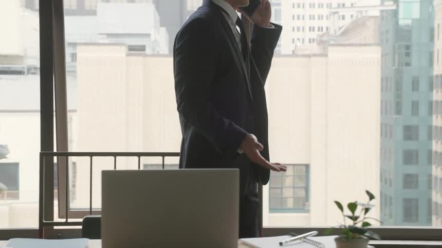Man in a suit talking on the phone in an office with a city view