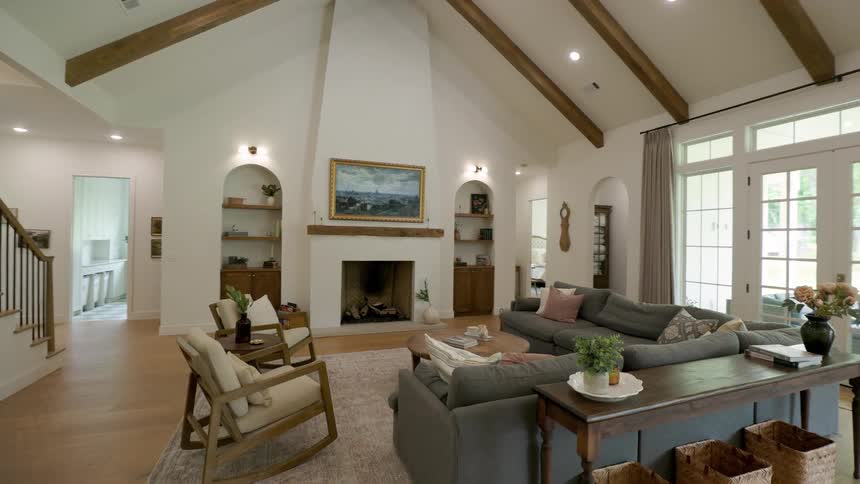 Spacious living room with vaulted ceiling and exposed beams centered around fireplace with artwork above