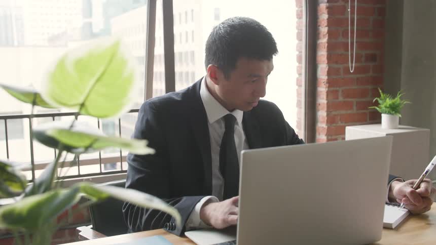 Man in a suit using a laptop in an office with a brick wall