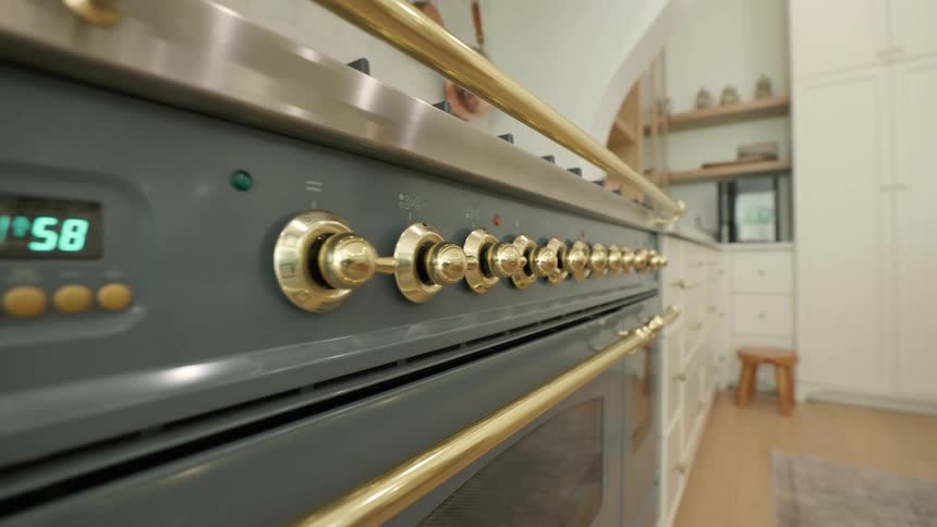 Highend stove with brass knobs in modern kitchen featuring white cabinets and light wood flooring