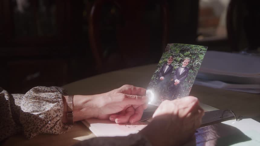 Hands hold photo of two youths in black suits with bow ties in front of green foliage