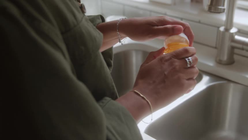Woman stands at the kitchen sink and opening a prescription medicine bottle and pouring pills into her hand