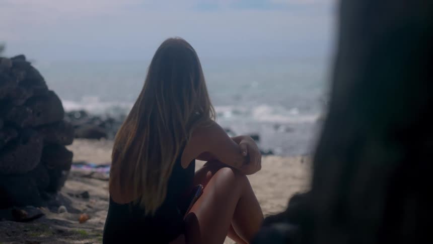 Woman sitting on the sand watches the sea in front of the stone structure