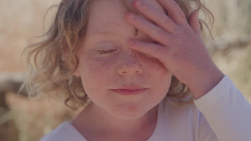 Child with curly hair and freckles raises hand beside the head