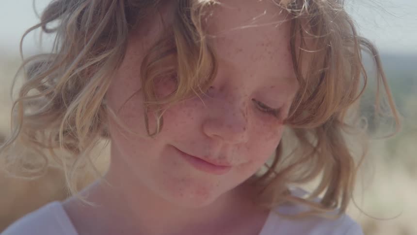 Child with curly hair and freckles looks downward with a slight smile