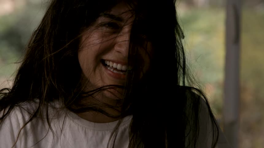 A young woman with long unkempt hair laughs excitedly indoors her lively energy filling the room