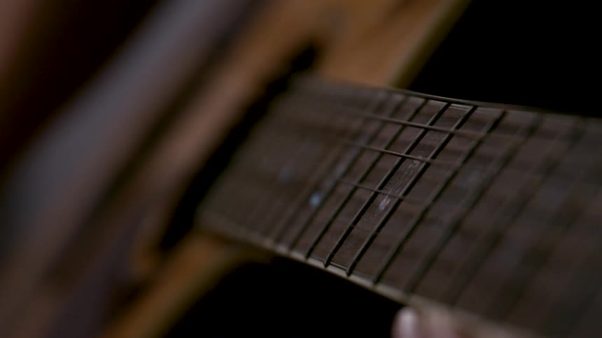 The strings of an acoustic guitar move across the fret board