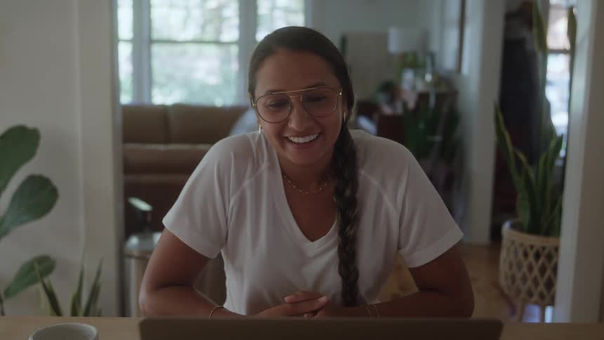 The woman is smiling and talking on her laptop