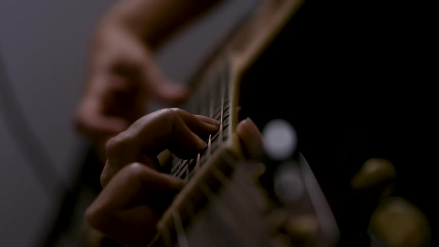 Hand presses strings on the guitar neck in softly lit setting