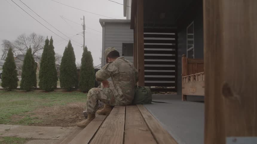 The soldier gets up from the porch and walks from the home