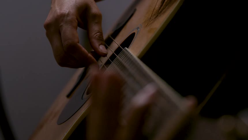 Man strums the strings of an acoustic guitar with his fingers on the fret board