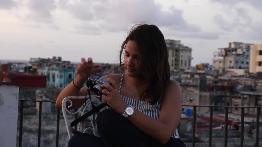 A woman holds a camera on a city rooftop