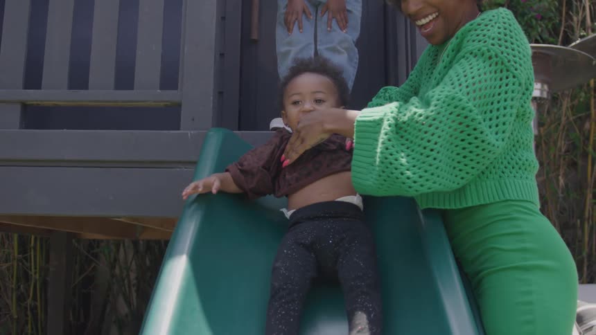 The mother pushes her daughter down the slide