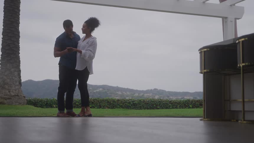 Woman and man look at an object together on a terrace overlooking hills and greenery