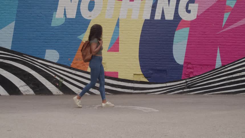 The woman walks past building with a mural painted on it
