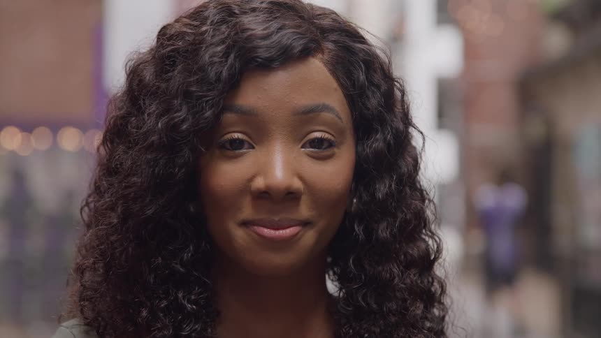 The woman with curly hair is smiling outside