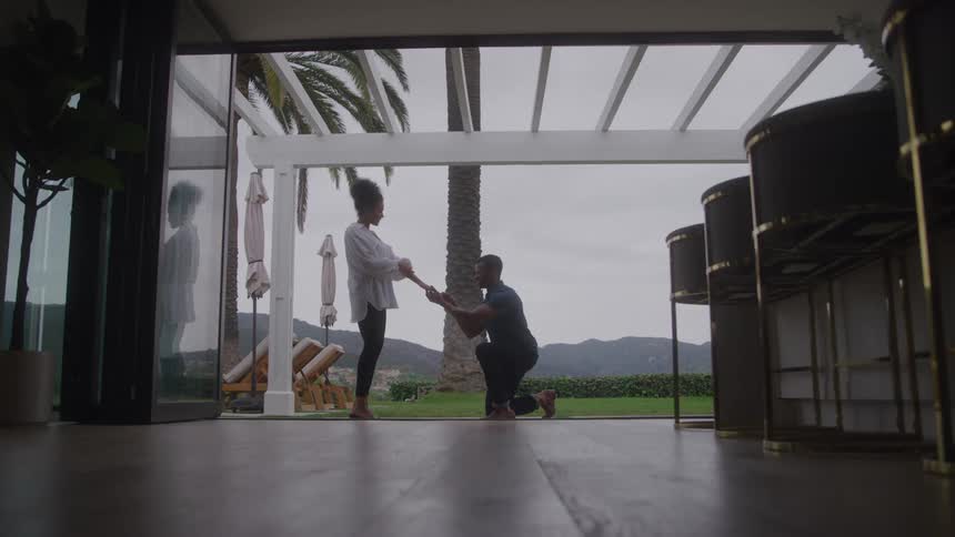 Young black man kneeling in front of a young black woman proposing marriage during day time