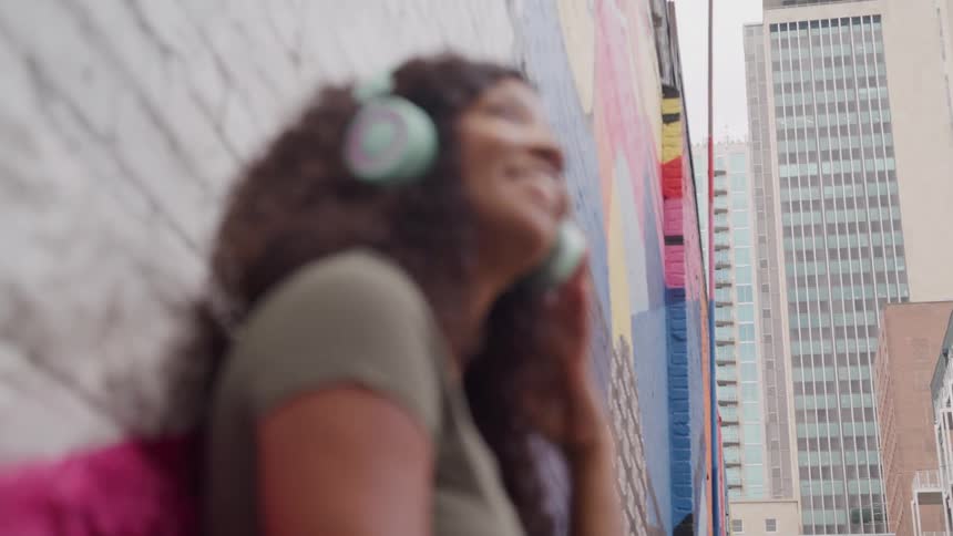 Young woman standing against a city building jamming with her headphones