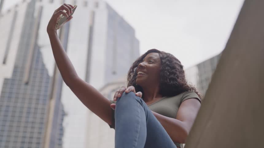 Young woman sitting outside holding up her phone taking a selfie