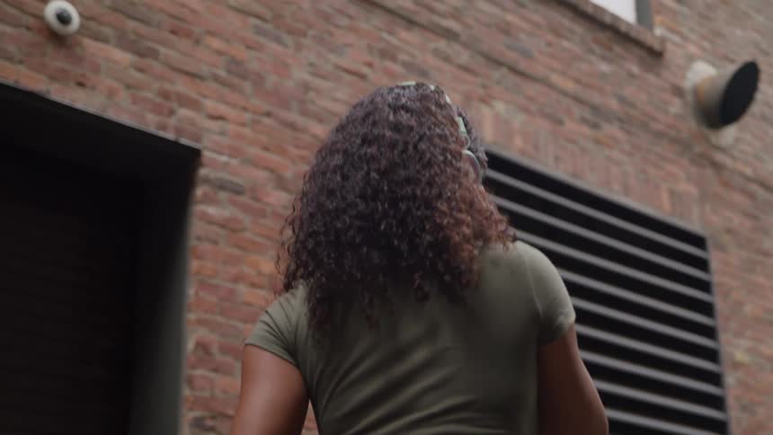 Young woman wearing headphones smiles walking around looking at neighborhood buildings