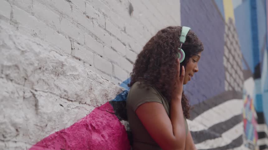 Young woman standing against a city building jamming with her headphones