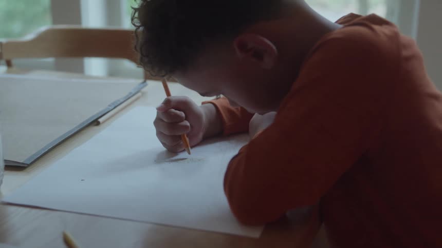 Boy leaning over the table drawing on paper
