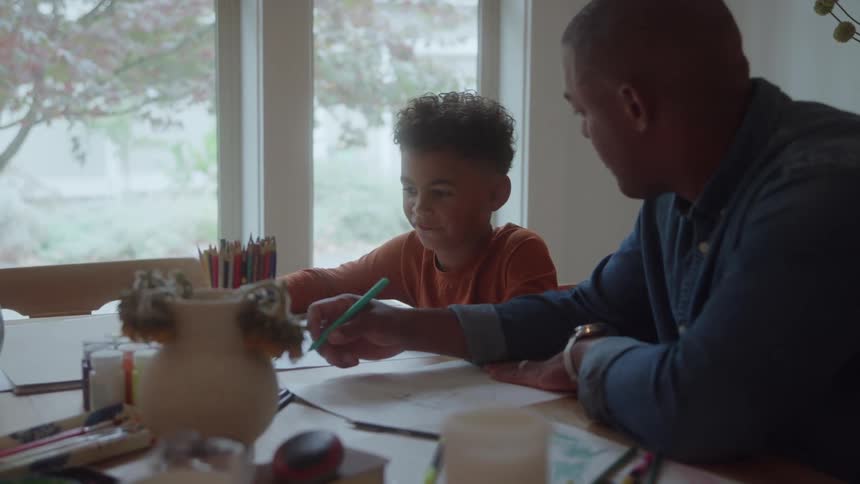 Man watches a child drawing on the table near the window