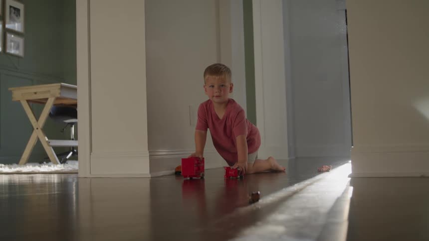 Little boy playing with his toys on the floor as sunlight shines through the window