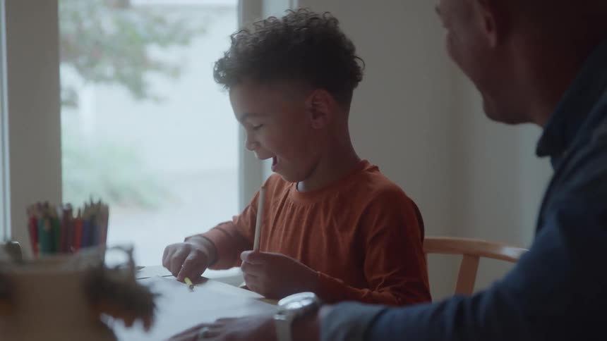 Boy sitting at the table handling pencils next to an adult