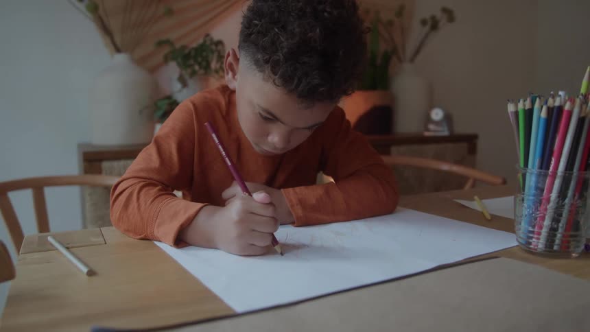 Child draws on a large sheet using colored pencils on the table