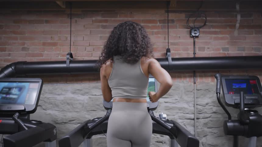 Curlyhaired person works out on treadmill in gym with brick walls and surrounding equipment