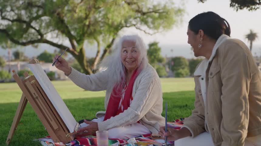 People sitting on a colorful blanket painting outdoors with a view of trees and mountains