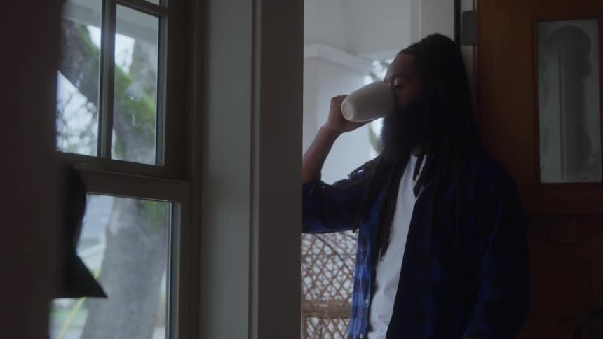 Man standing in the hallway leaning against the wall drinking a cup of coffee