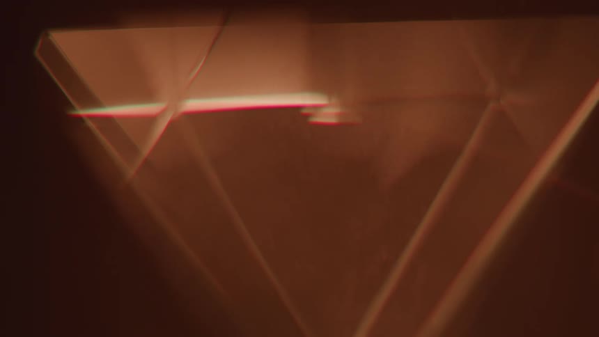 A close abstract view of a prism with sharp triangular facets rotating against a brown background creating warm light reflections and chromatic aberration