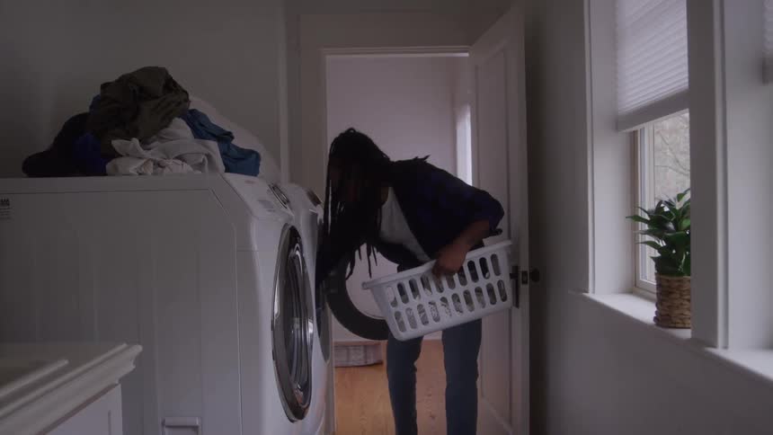 A woman leans down to remove laundry from the dryer and place in a basket