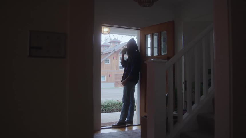Man standing in the front doorway of his house drinking a cup of coffee